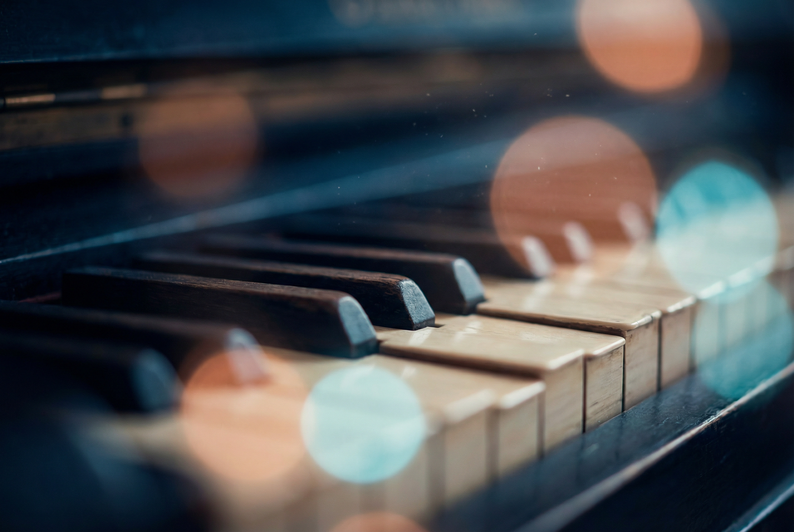 Piano keys with warm copper and cyan bokeh lighting — the aesthetic of David Warrick Media's studio